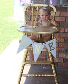 a baby sitting in a high chair with a banner on it's back that says one