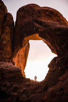 two people standing in the middle of an arch shaped rock formation with snow falling on them