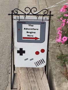 a sign that says the adventure begins here with a gameboy design on it and an arrow pointing up