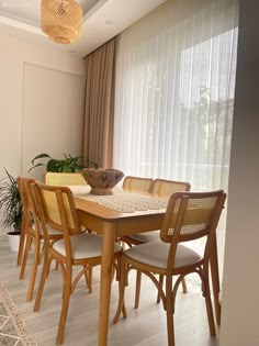 a dining room table and chairs in front of a window with sheered drapes