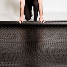 a man kneeling down on top of a black piece of rubber flooring with his hands in the air