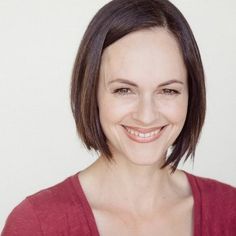 a smiling woman in a red shirt is looking at the camera and she has short brown hair