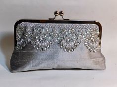 Absolutely stunningly beautiful dupioni silk silver clutch with silver lace.   It is embellished with silver rhinestones and pearls.  It comes with silver satin lining and silver/nickel frame.Fabric: Dupioni SilkLining: satinTwo layers of interlining and battingSilver/nickel kisslock frameTop Width 8"Bottom Width 9"Height 5 1/2"Reinforced stitching for durability*Note:  A chain can be added for $4.00.  Please see my chain listing.*The metal purse frame is made of iron with a nickel-free finish. Luxury Silver Evening Bag With Removable Pouch, Luxury Clutch Flap Bag With Silver-tone Hardware, Luxury Silver Handheld Clutch, Luxury Clutch With Silver-tone Hardware For Events, Luxury Clutch With Silver-tone Hardware For Formal Occasions, Luxury Silver Embroidered Bag, Luxury Clutch Evening Bag With Silver-tone Hardware, Luxury Silver Pouch Evening Bag, Luxury Evening Box Bag With Silver-tone Hardware