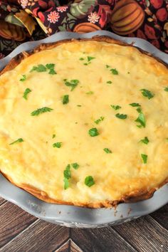 a cheesy quiche with parsley on top in a pie pan sitting on a wooden table