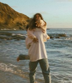 a woman walking along the beach with her dog on her back while she is holding an animal in her arms