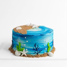 a cake decorated with sand, seaweed and starfish on a white tablecloth