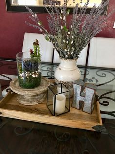 a glass table topped with a vase filled with flowers next to a candle on top of a wooden tray