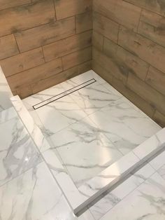 a white marble shower with wooden walls and flooring in a bathroom that looks like it has been remodeled