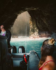 two people on a boat in front of a cave with blue water and light coming from it