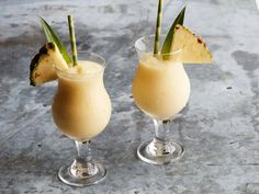 two glasses filled with ice cream and topped with pineapple wedges on a table