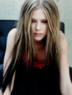 a woman with long blonde hair sitting on a black chair and looking at the camera