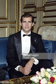 a man in a tuxedo sitting on a blue couch with flowers around him