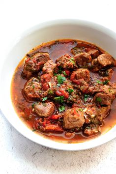 a white bowl filled with meatballs and tomato sauce on top of a marble counter