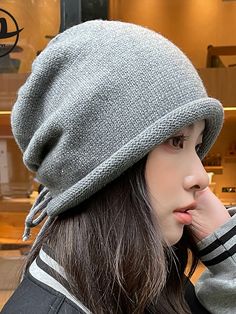 a woman wearing a gray hat with fringes on it's brim and her hand under her chin