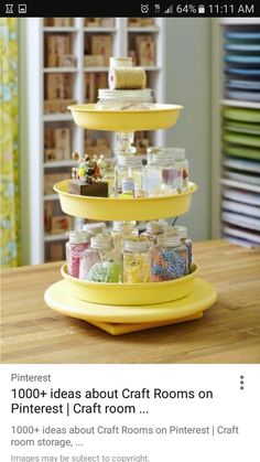 a three tiered tray holds jars and other craft supplies on a table in front of shelves