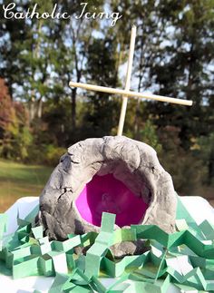 a cross on top of a rock with green paper around it and a pink bowl in the middle