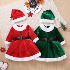 two children's christmas dresses and santa hats on a wooden floor next to decorations