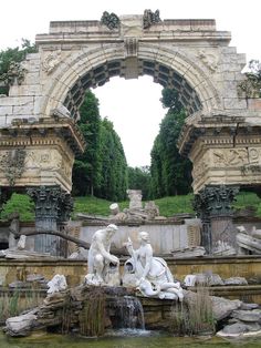 a fountain with statues in the middle of it and an archway leading to another area