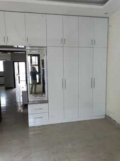 an empty room with white cupboards and a man taking a photo in the mirror