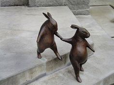 two bronze rabbits touching each other with their hands