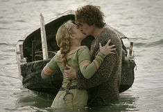 a man and woman kissing in the water next to a boat