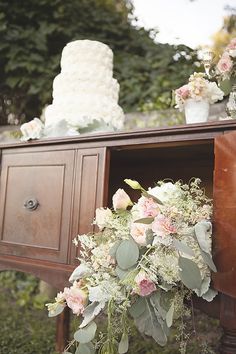 a wedding cake sitting on top of a wooden table next to flowers and greenery