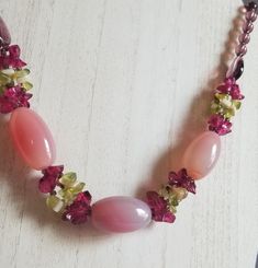 This vintage necklace is adorned with pink art glass beads, peridot and garnet colored chips.  There are three pink art glass beads and purple beads on each side at the top.  It makes a great collection piece or to wear it would make an outfit stand out. Pink Faceted Beads Gems And Cabochons For Gifts, Pink Czech Glass Beaded Necklace For Gifts, Pink Beaded Czech Glass Necklace, Pink Czech Glass Necklaces With Faceted Beads, Pink Czech Glass Necklaces With Colorful Beads, Pink Gemstone Beads For Jewelry Making, Pink Faceted Beads For Jewelry Making, Handmade Pink Czech Glass Necklaces, Handmade Pink Czech Glass Necklace