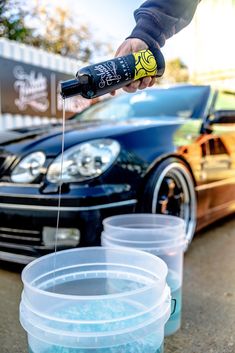 a car being filled with blue liquid by a person pouring it into two plastic containers