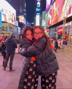 two girls hugging each other in the middle of a busy city street at night time