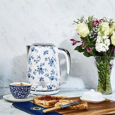 a table topped with a glass vase filled with flowers next to a toaster and knife