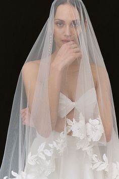 a woman wearing a wedding veil with white flowers on it and her hand under her chin