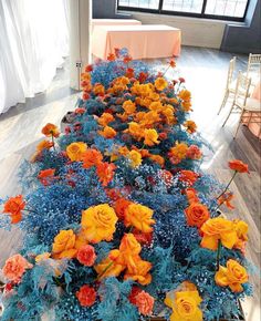 an arrangement of orange and blue flowers on a long table with chairs in the background