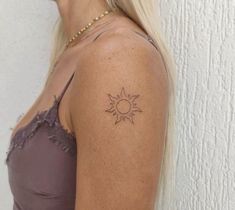 a woman with a small sun tattoo on her left shoulder and right arm, standing against a white wall