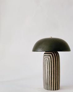 a black and white striped vase with a green lamp on the top, against a white background