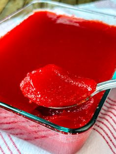 a spoon full of red sauce sitting on top of a glass dish filled with liquid