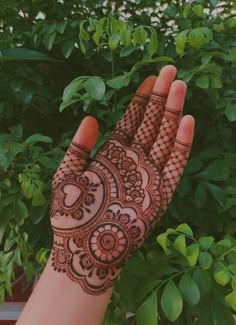 a hand with henna on it and green plants in the background, all around