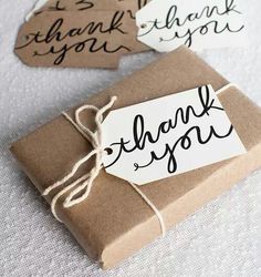 two brown paper tags with thank you written on them sitting next to a wrapped gift