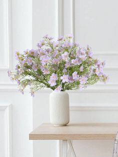 a white vase filled with purple flowers on top of a wooden table