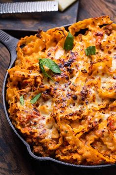 a casserole dish with cheese and meat in it on a wooden table next to a knife