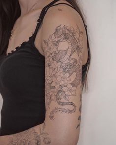 a woman with a dragon and flowers tattoo on her arm is standing in front of a white wall