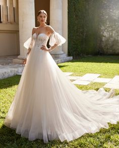 a woman in a wedding dress standing on the grass with her hands on her hips