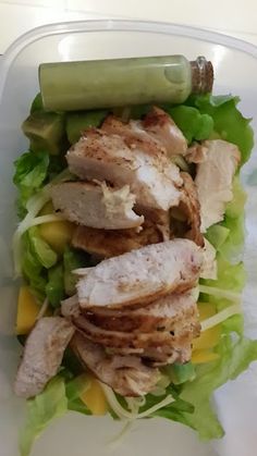 a plastic container filled with lettuce, meat and other food items on top of it