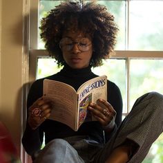 a woman reading a book in front of a window