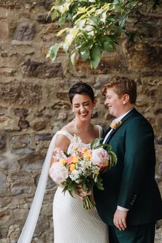 a bride and groom standing in front of a stone wall