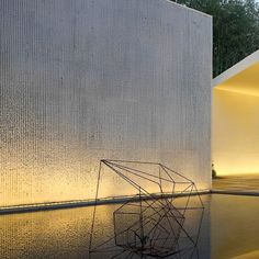 an artistic sculpture in front of a building with water reflecting off it's surface