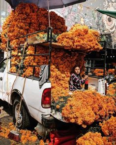 a truck is loaded with orange flowers and people are looking at the flower arrangement in the back