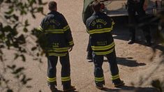 two fire fighters standing in front of a truck on the side of a dirt road