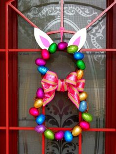 an easter wreath with bunny ears and colorful eggs on the front door, hanging from a red metal frame