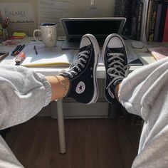 two people sitting at a desk with their feet up on the table and one is wearing converse shoes