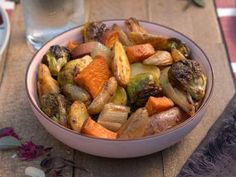 a bowl filled with vegetables sitting on top of a wooden table next to a glass of water